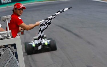 Ferrari's Formula One driver Felipe Massa, of Brazil, waves flag as Brawn GP's Jenson Button, of Britain, approaches the finish line to win the 2009 F1 World Championship by arriving fifth at the Brazilian F1 Grand Prix, on the Interlagos racetrack in Sao Paulo, Sunday, Oct. 18, 2009. (AP Photo/Luca Bruno)