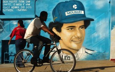 People pass by a painting of Brazilian F1 champion Ayrton Senna in Sao Paulo, Brazil, on Friday, April 30, 2004. Senna died following his fatal car crash at Imola track, Italy, on May 1, 1994. The writing in the wall reads "Every F1 driver has a limit. Mine is a little bit higher", in words supposedly spoken by Ayrton Senna. (AP Photo/Alexandre Meneghini)